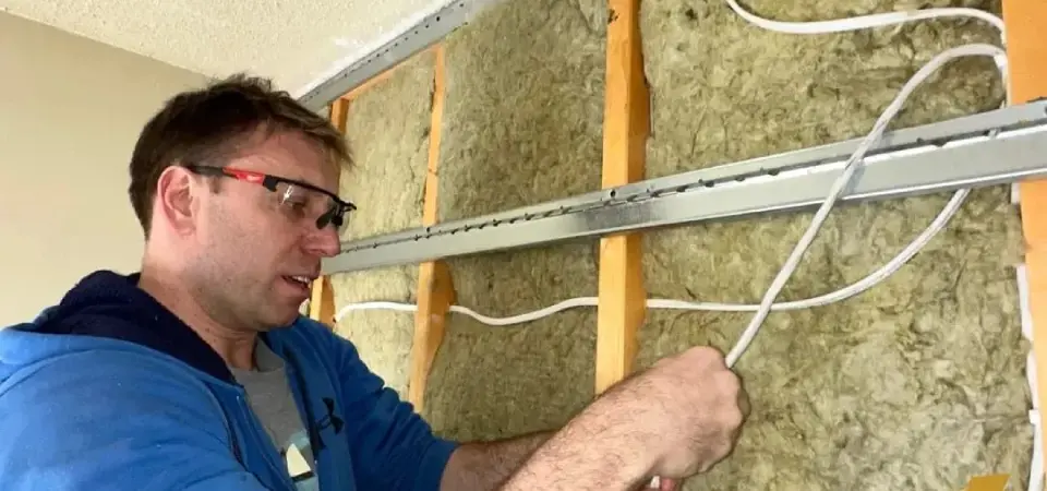 Man installing wires in wall insulation.